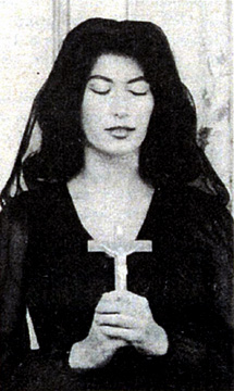 Sexy, young woman donned entirely in black, gown, hair and very deep in prayer holding crucifix