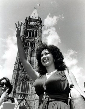 Skyline, bottom - up view of sexy, huge breasted stripper in white rosary in front of the Peace Tower of the Canandian Parliament building.